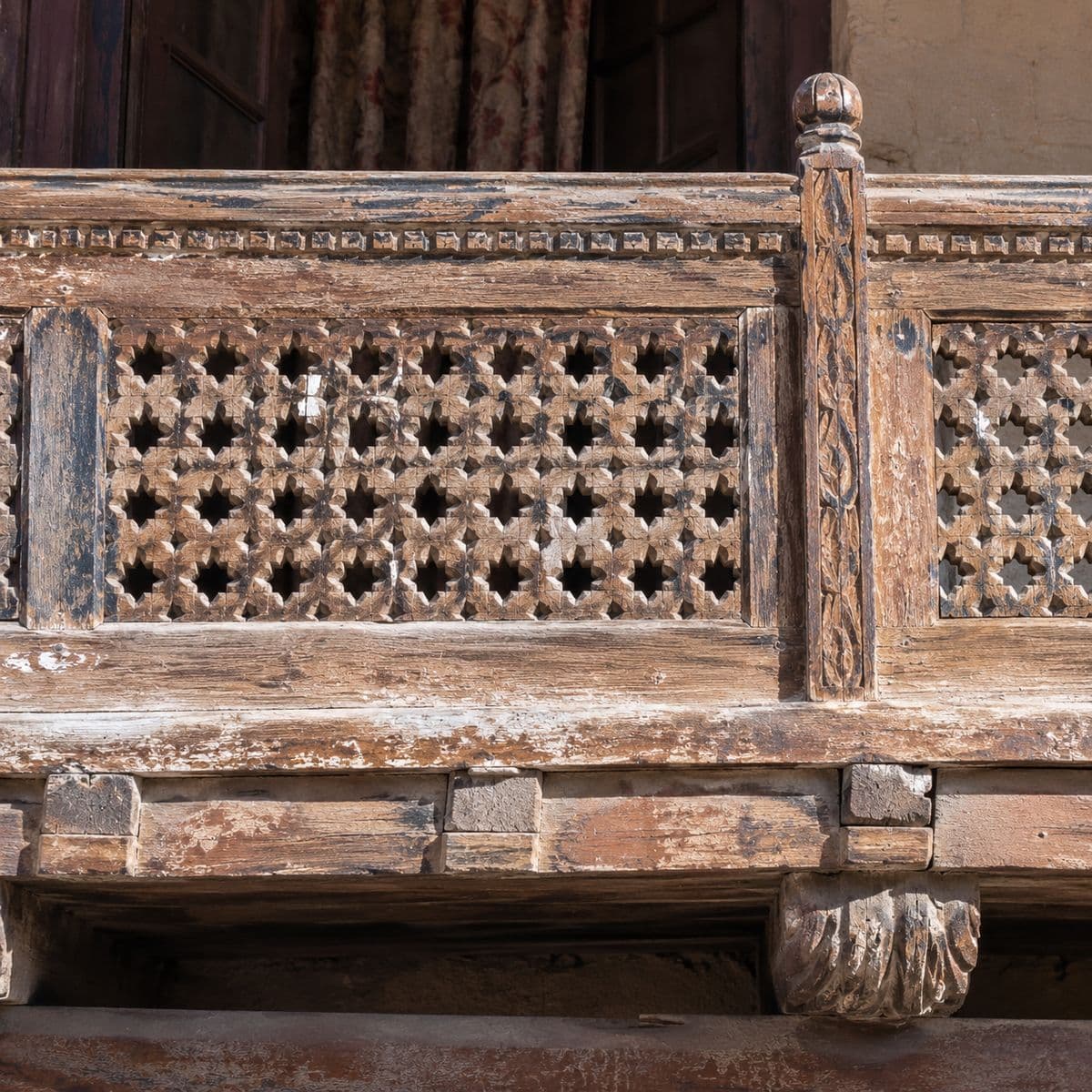 A carved and pierced timber balcony rail with a turned baluster, weathered pale by sun.
