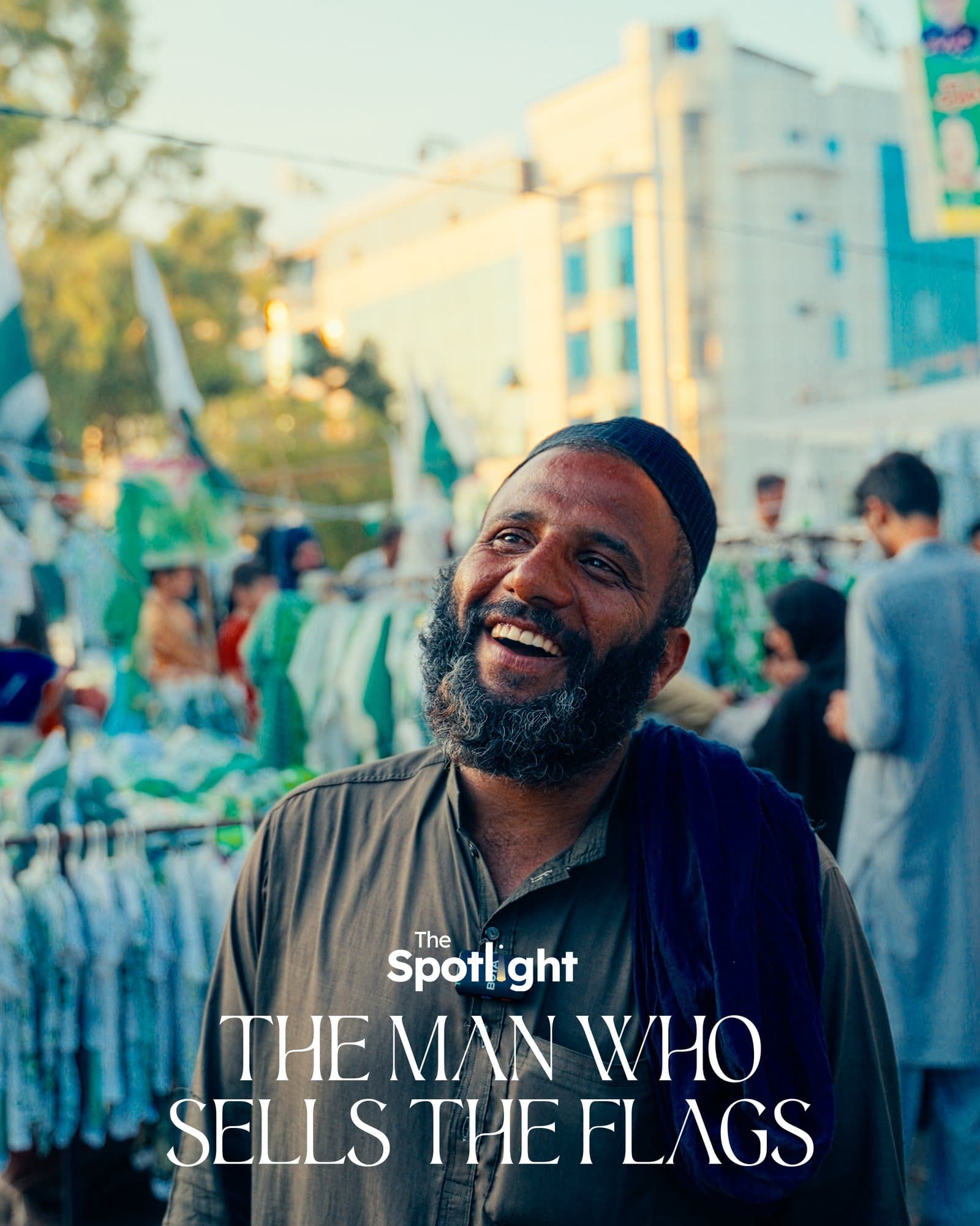 A man smiling in front of a street stall hung with green and white flags and bunting.
